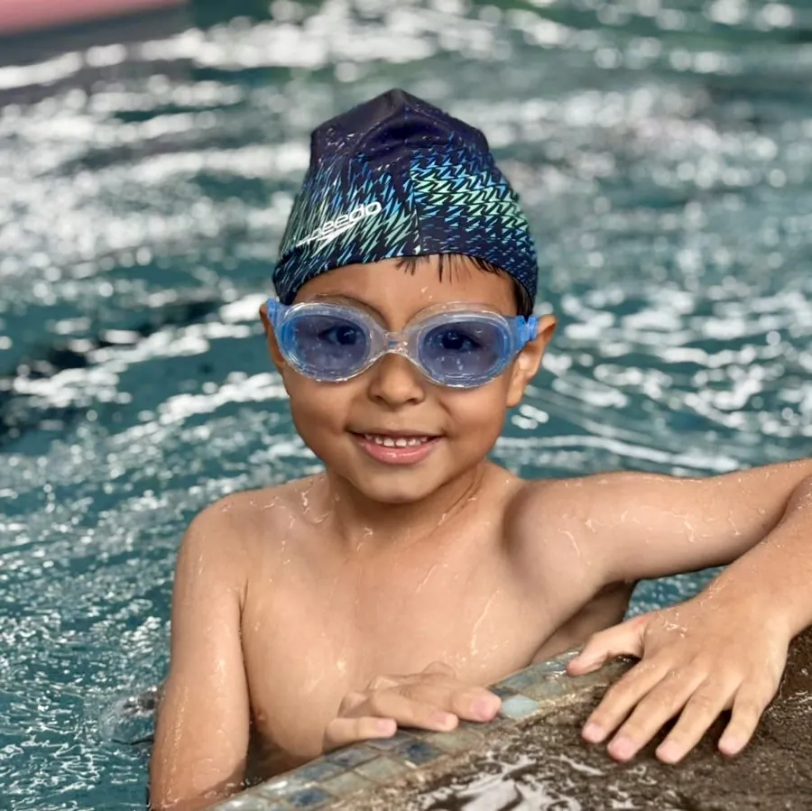 Niño sonriendo en la orilla de la piscina con gorro y goggles